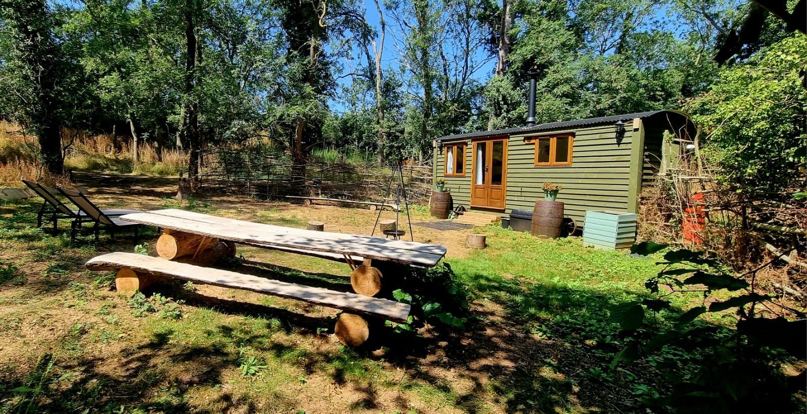An en-suite shepherd's hut at The Apple Farm with a picnic bench in dappled summer woodland, included in exclusive-use group glamping in Warwickshire