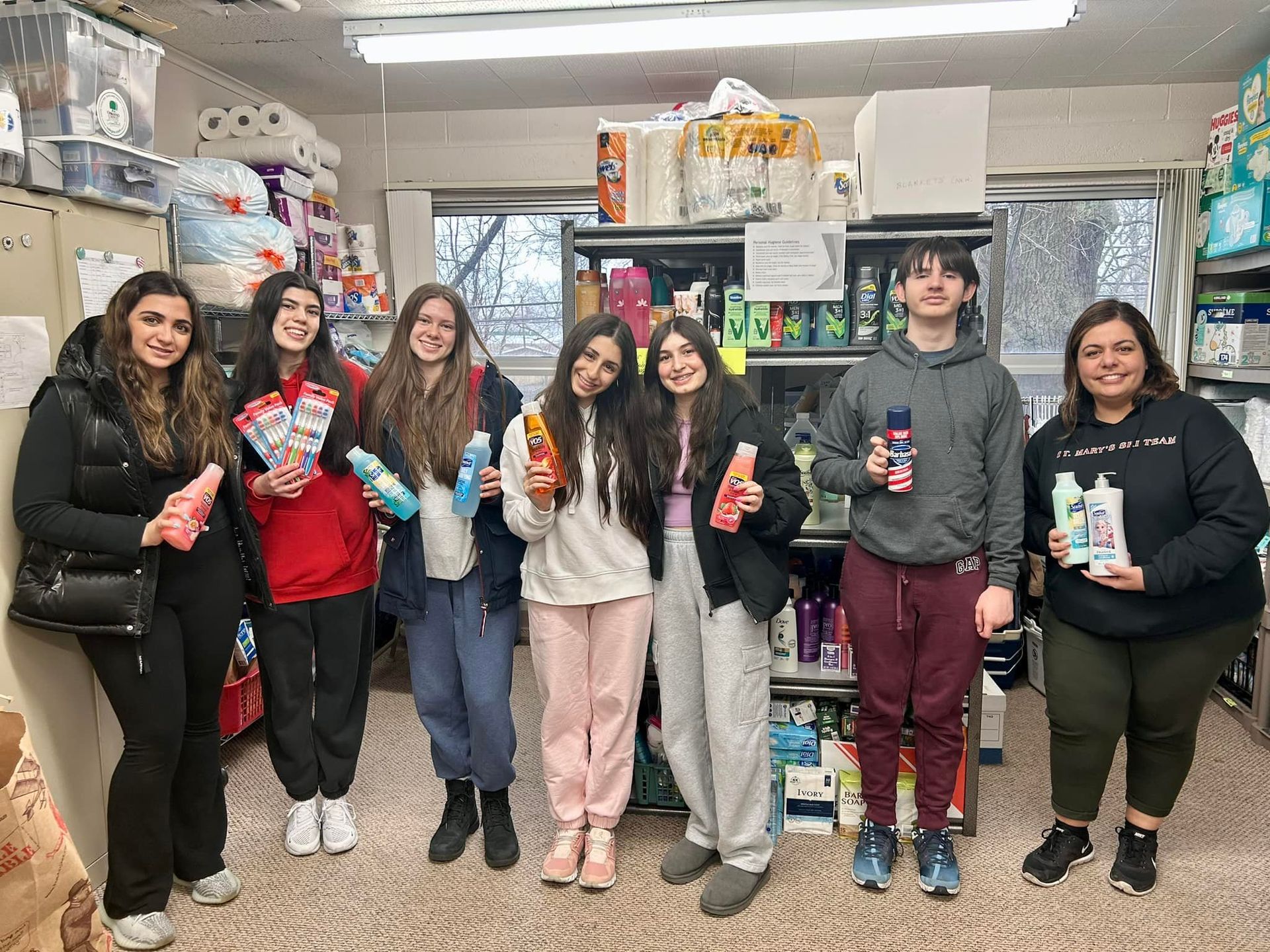 Group of people holding toiletries in a donation center, smiling.