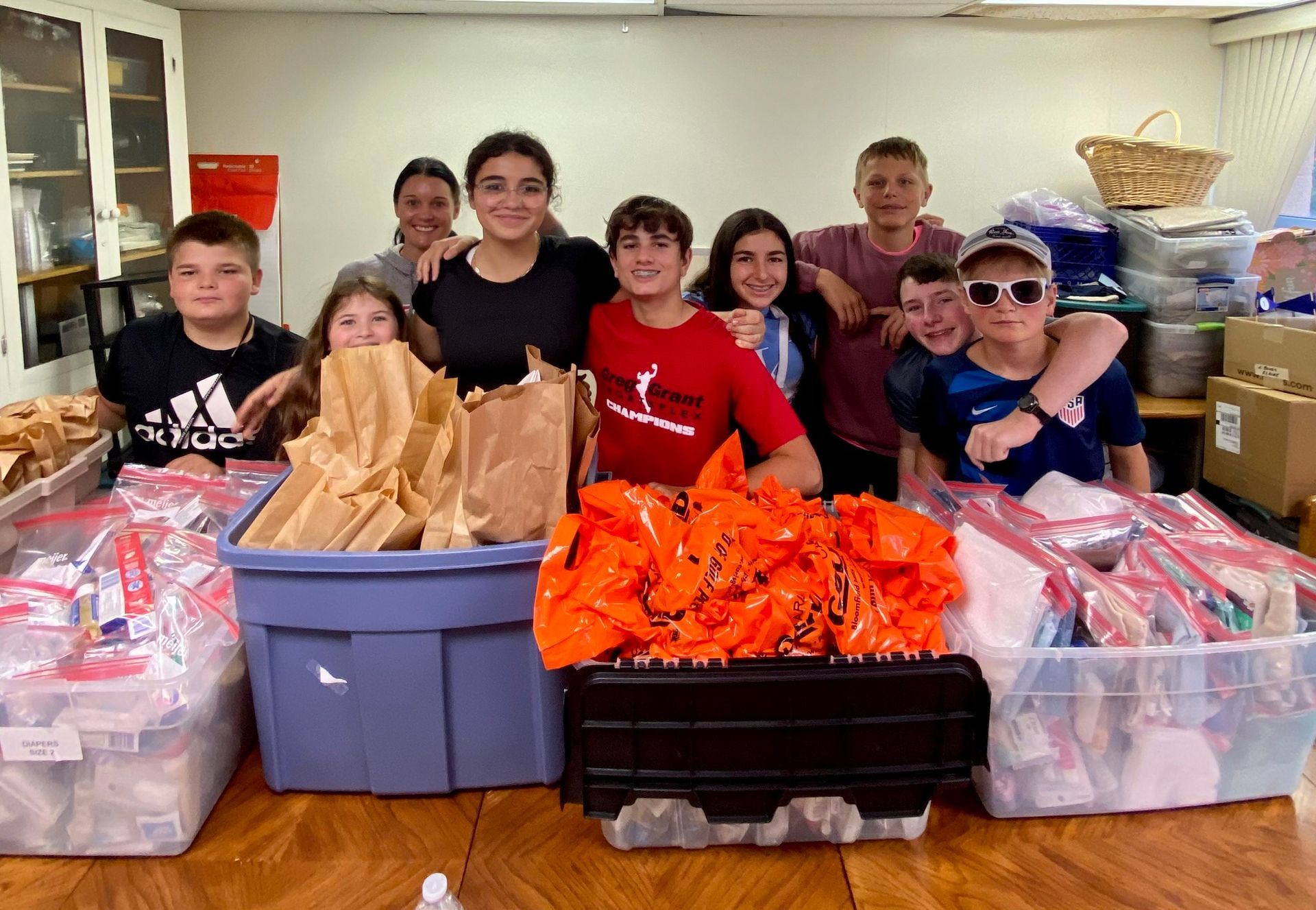 Group of children smiling with bags of food, likely for charity, at a table.