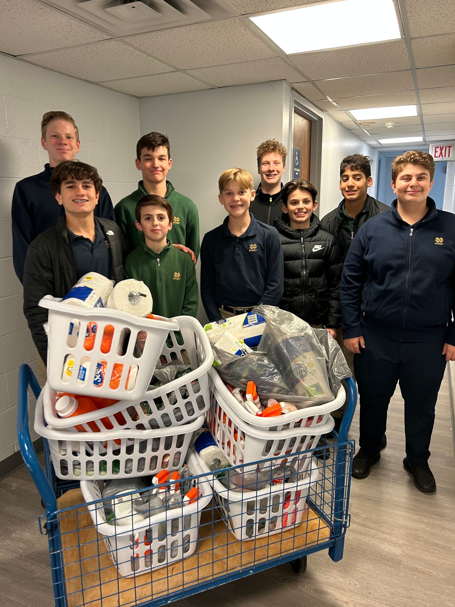 Group of students with baskets of supplies on a cart, in a hallway.