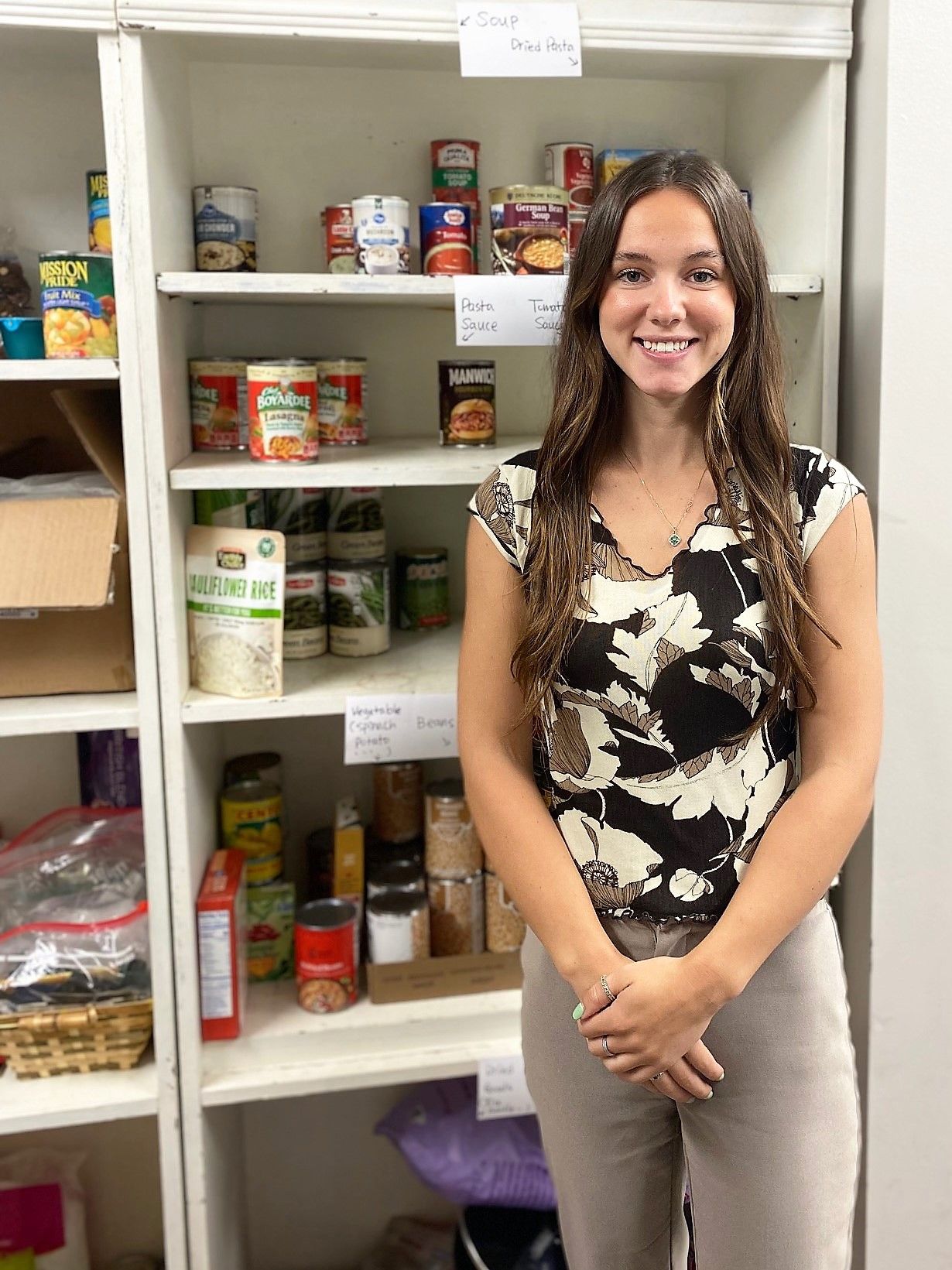 Woman standing near a pantry shelf with canned goods, smiling.