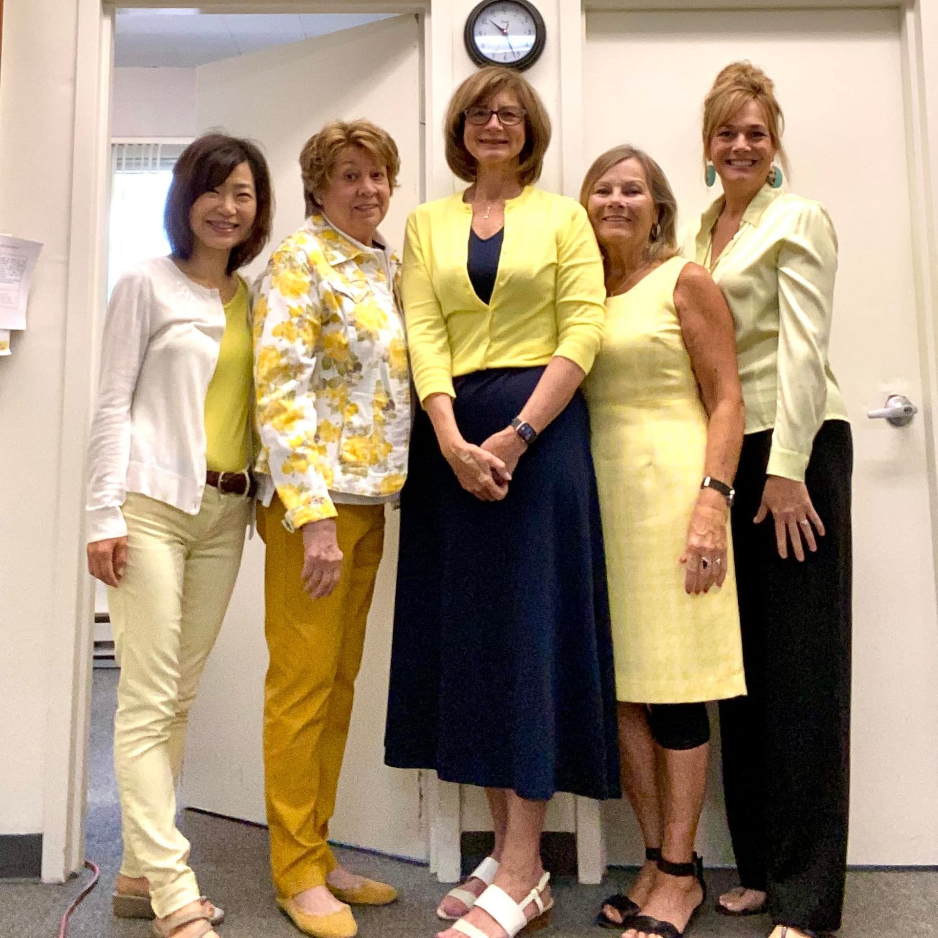 Five people in a doorway, all wearing yellow clothing, posing for a photo.