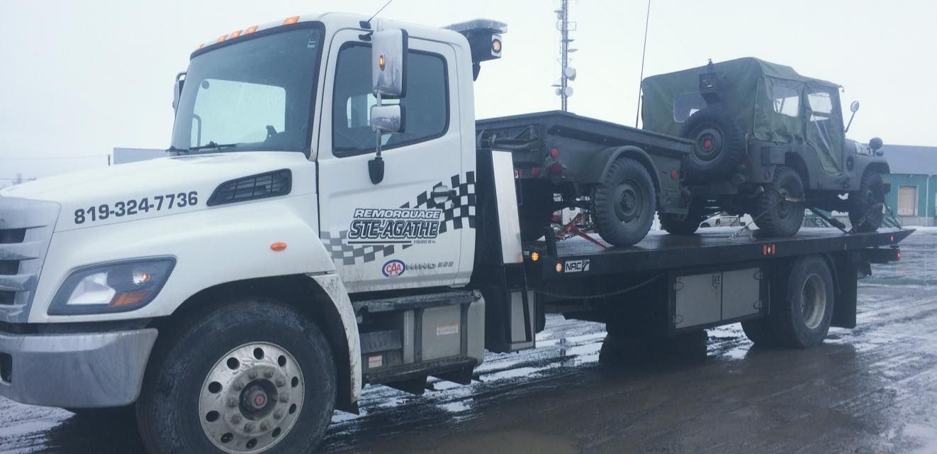 Une dépanneuse transporte un véhicule militaire à l'arrière.