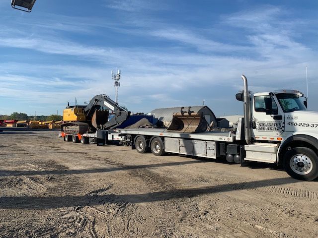 Une dépanneuse transporte une grosse excavatrice sur une remorque à plateau.