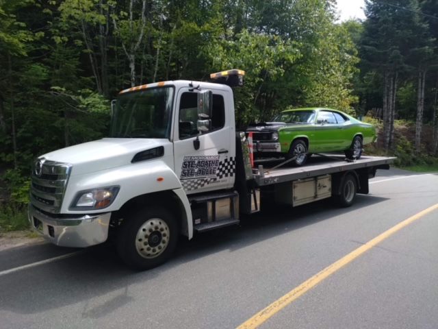 Une dépanneuse transporte une voiture verte à l'arrière.