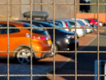 Une rangée de voitures est garée dans un parking derrière une clôture en fil de fer.