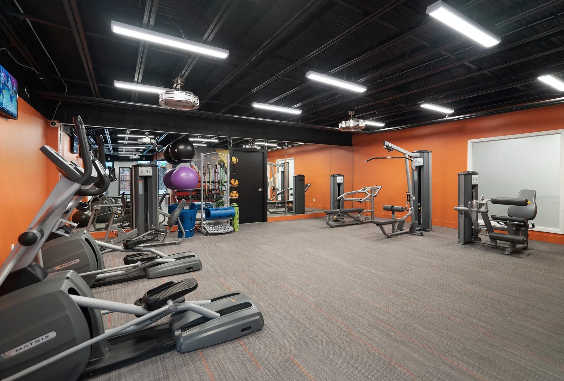 Interior of a modern gym with cardio and strength equipment against orange walls.