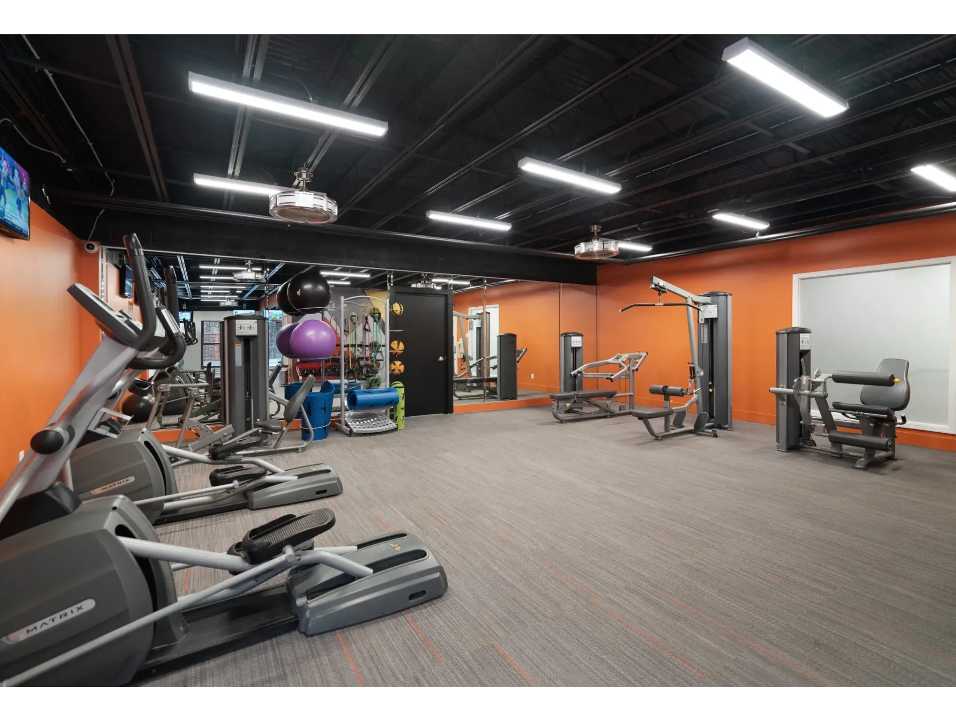 Interior of a modern gym with cardio and strength equipment against orange walls.