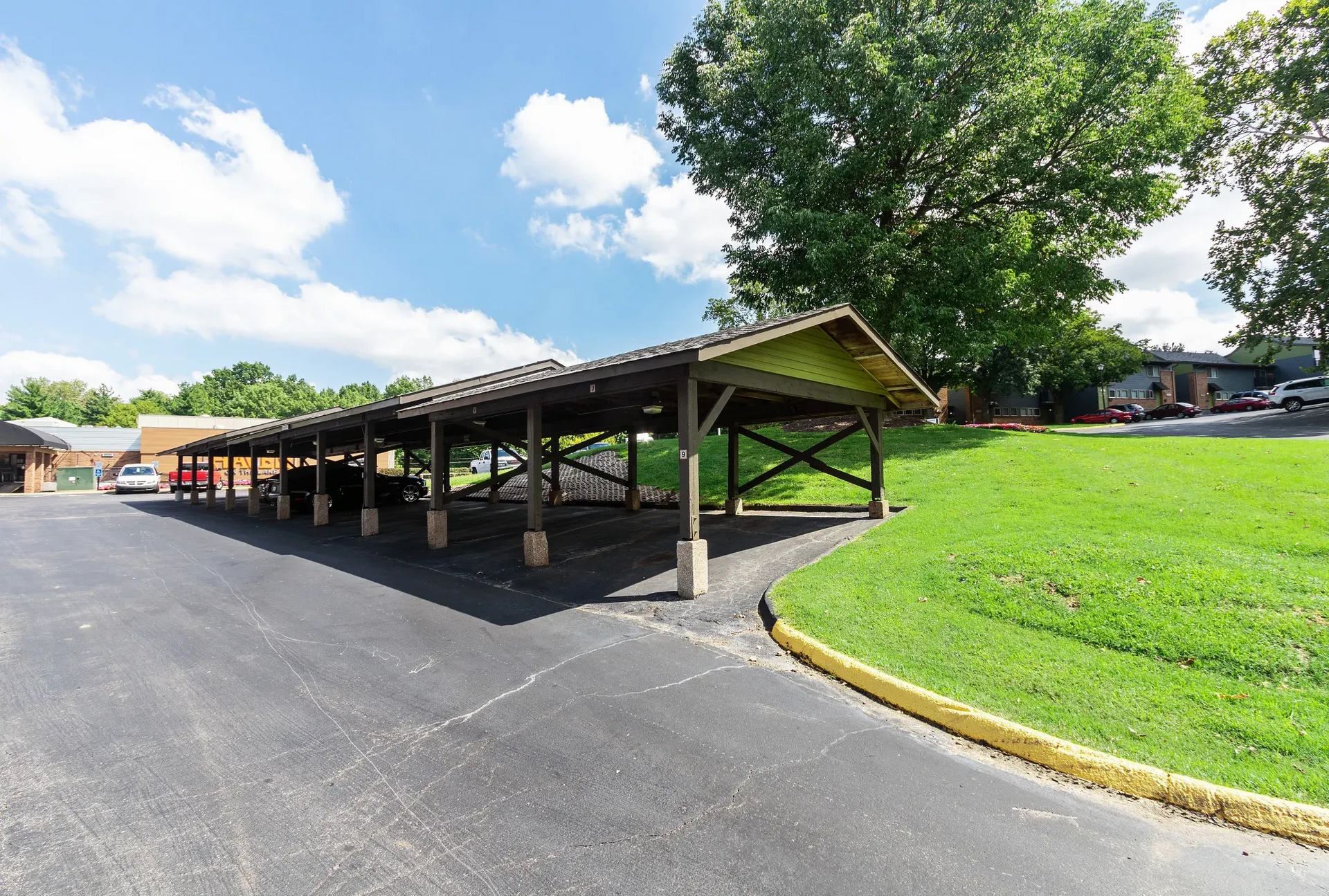 Covered carport with multiple parking stalls and cars beside a grassy slope.