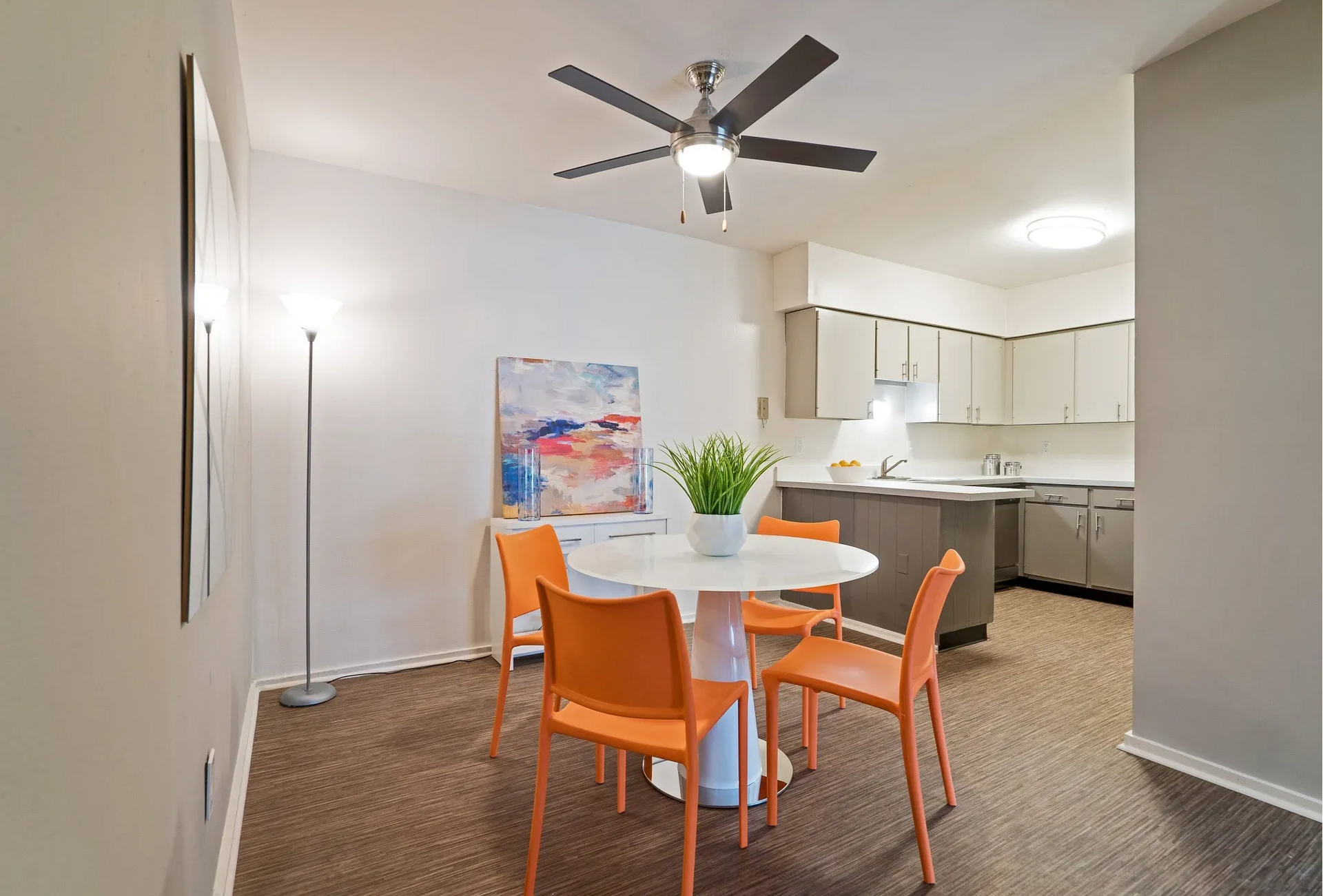 Open-concept dining area with round white table and orange chairs near the modern kitchen.