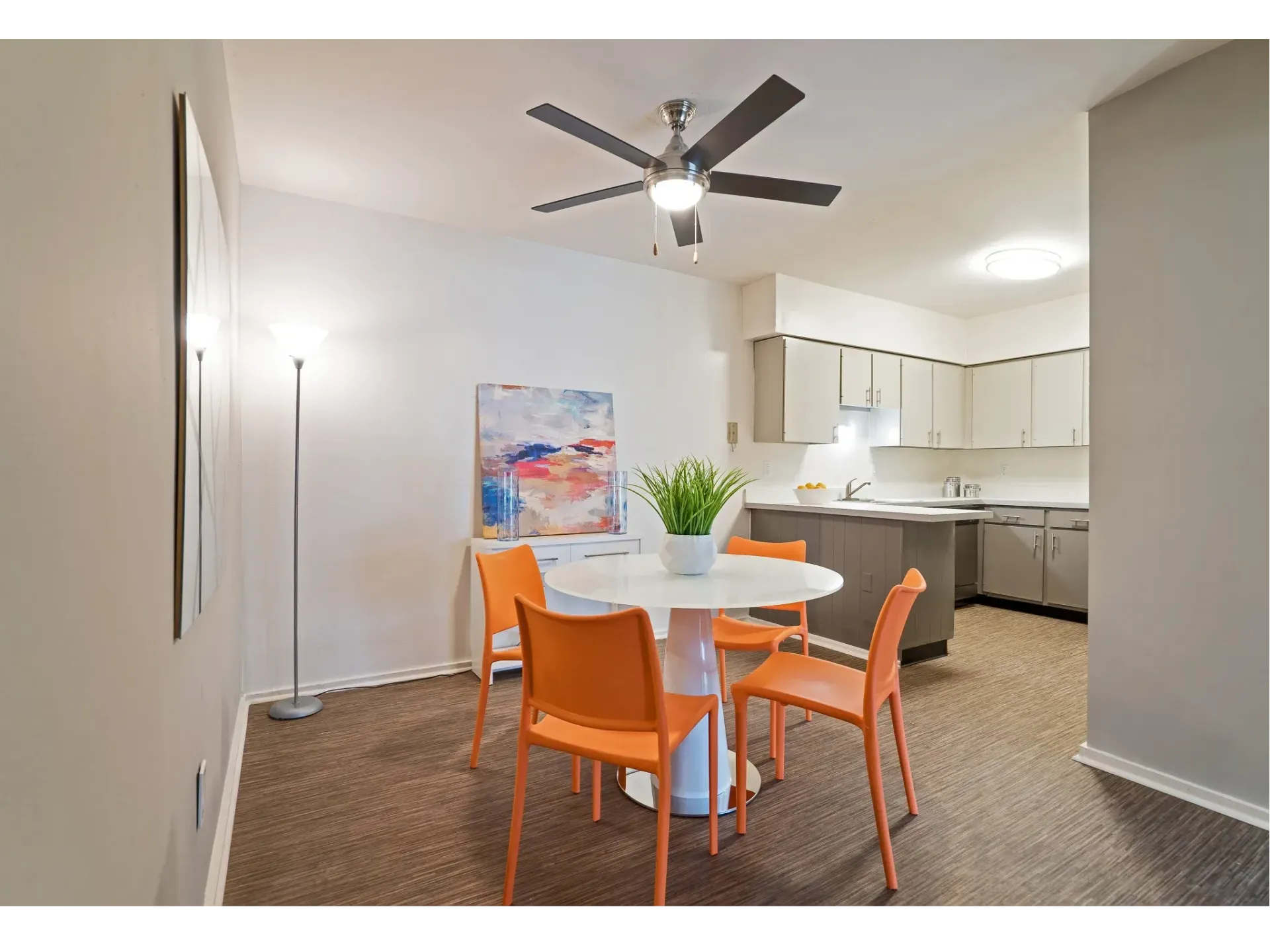 Open-concept dining area with round white table and orange chairs near the modern kitchen.