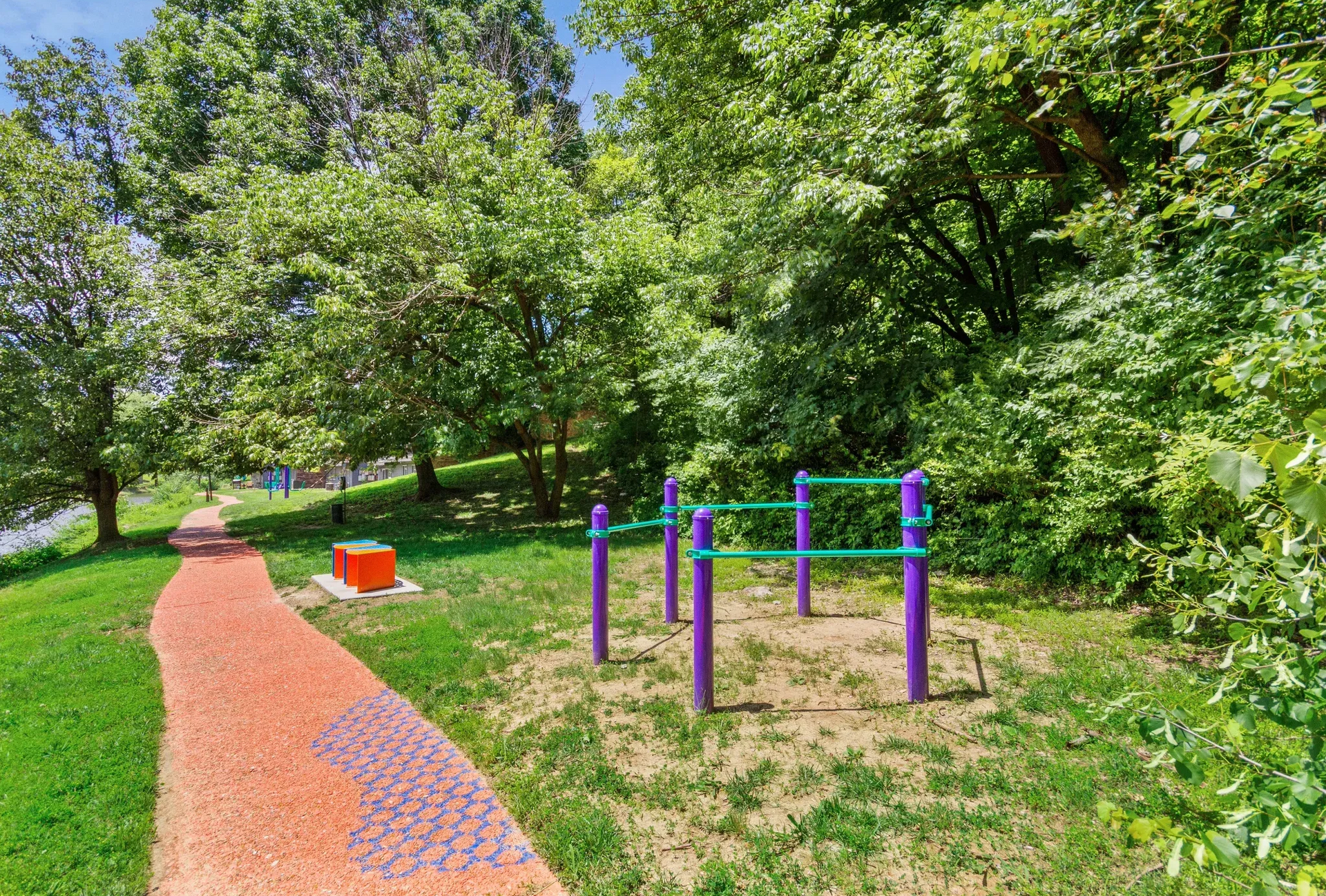 Outdoor fitness area with purple workout bars along a red winding path under trees.