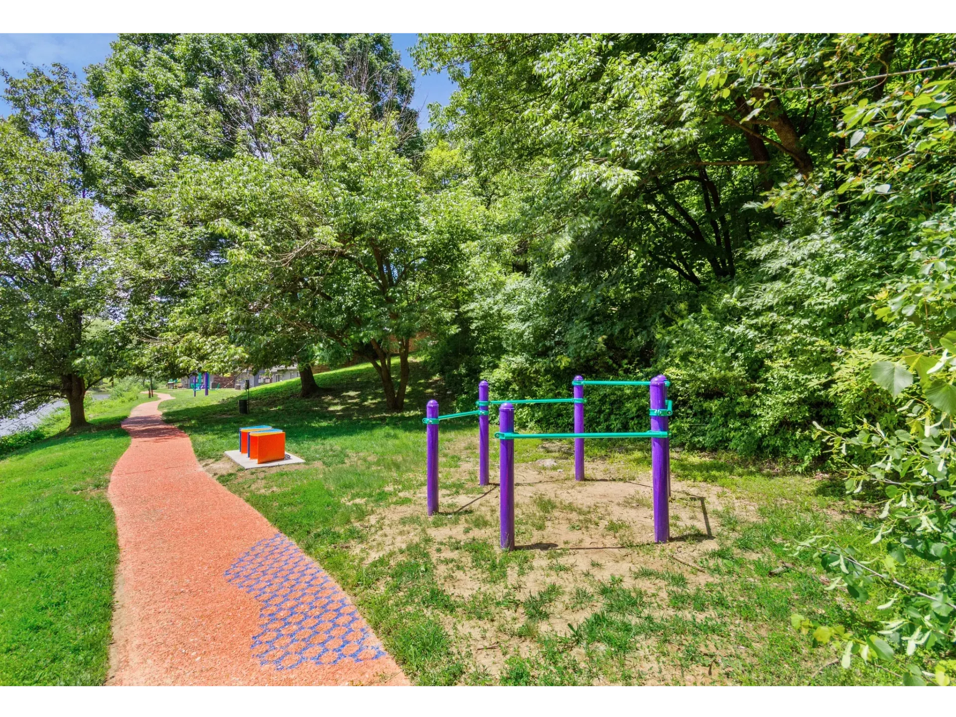 Outdoor fitness area with purple workout bars along a red winding path under trees.
