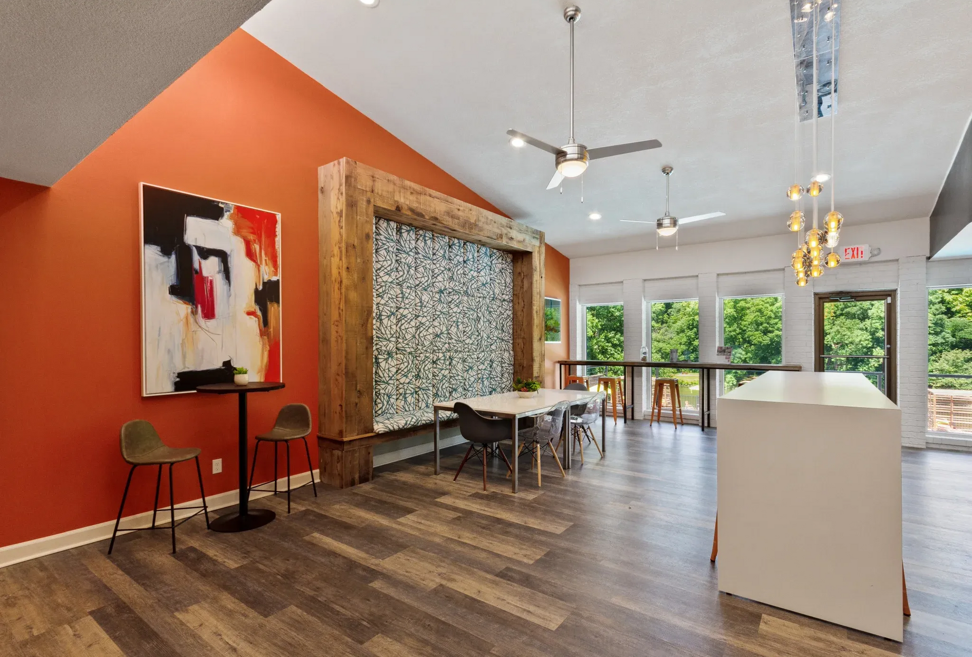 Interior of a communal lounge with orange wall, artwork, wood flooring, and seating.