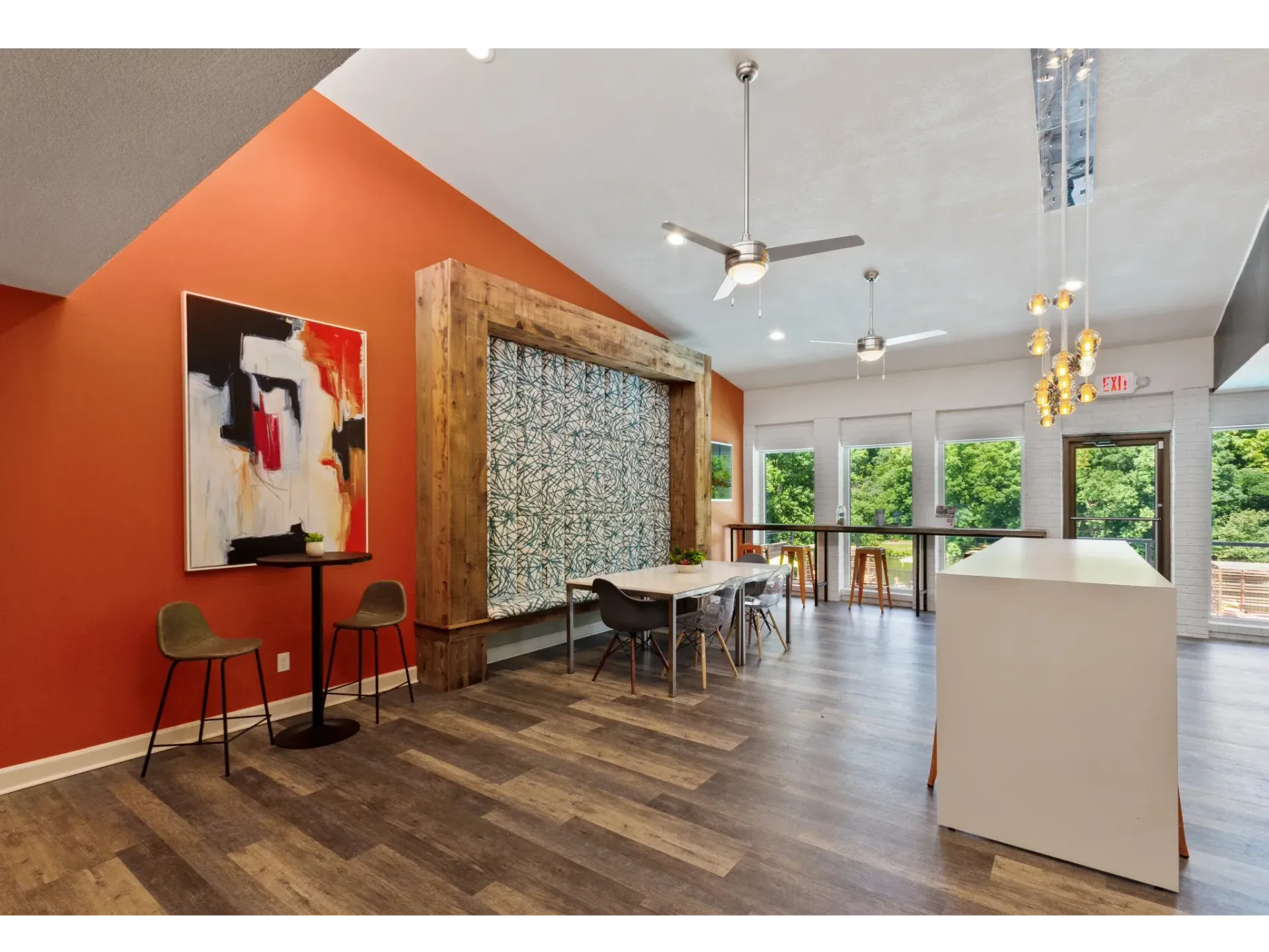 Interior of a communal lounge with orange wall, artwork, wood flooring, and seating.