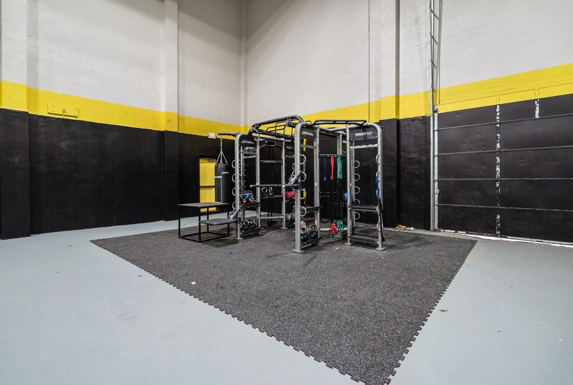 Indoor community gym with weight racks, mat area, and boxing bag.
