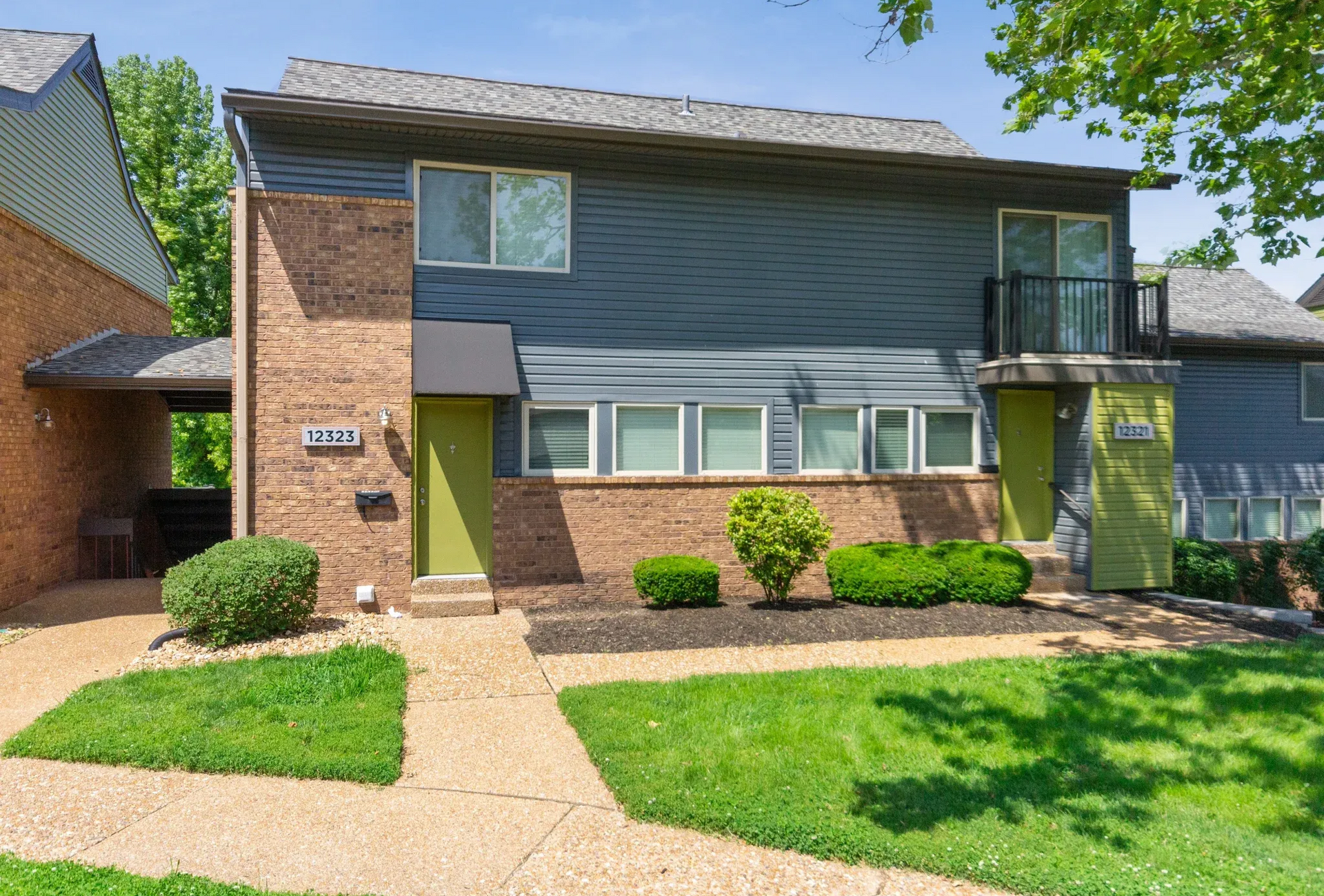 Two-story blue siding apartment building with brick accents and green entry doors, landscaped front.
