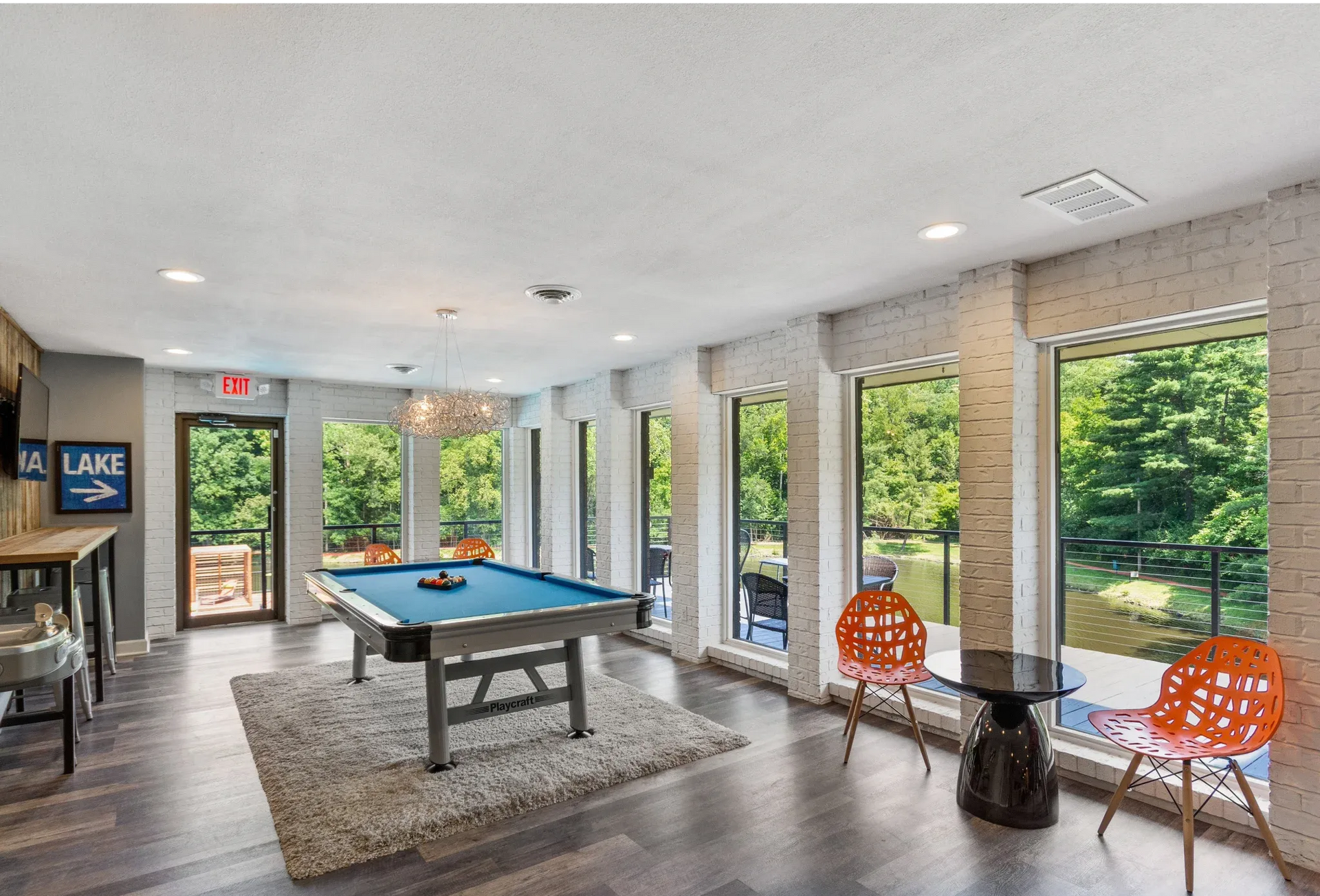 Indoor community recreation room with a pool table, rug, and large windows overlooking greenery.