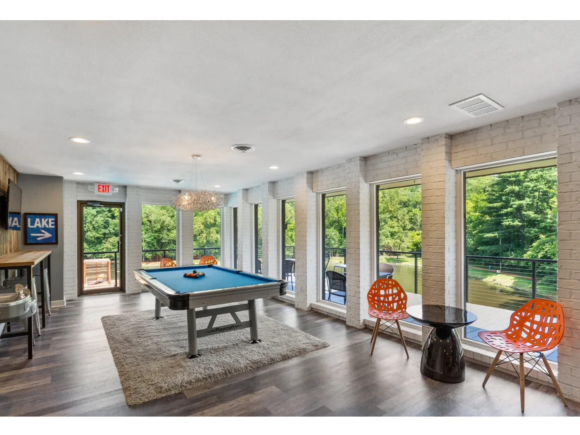 Indoor community recreation room with a pool table, rug, and large windows overlooking greenery.