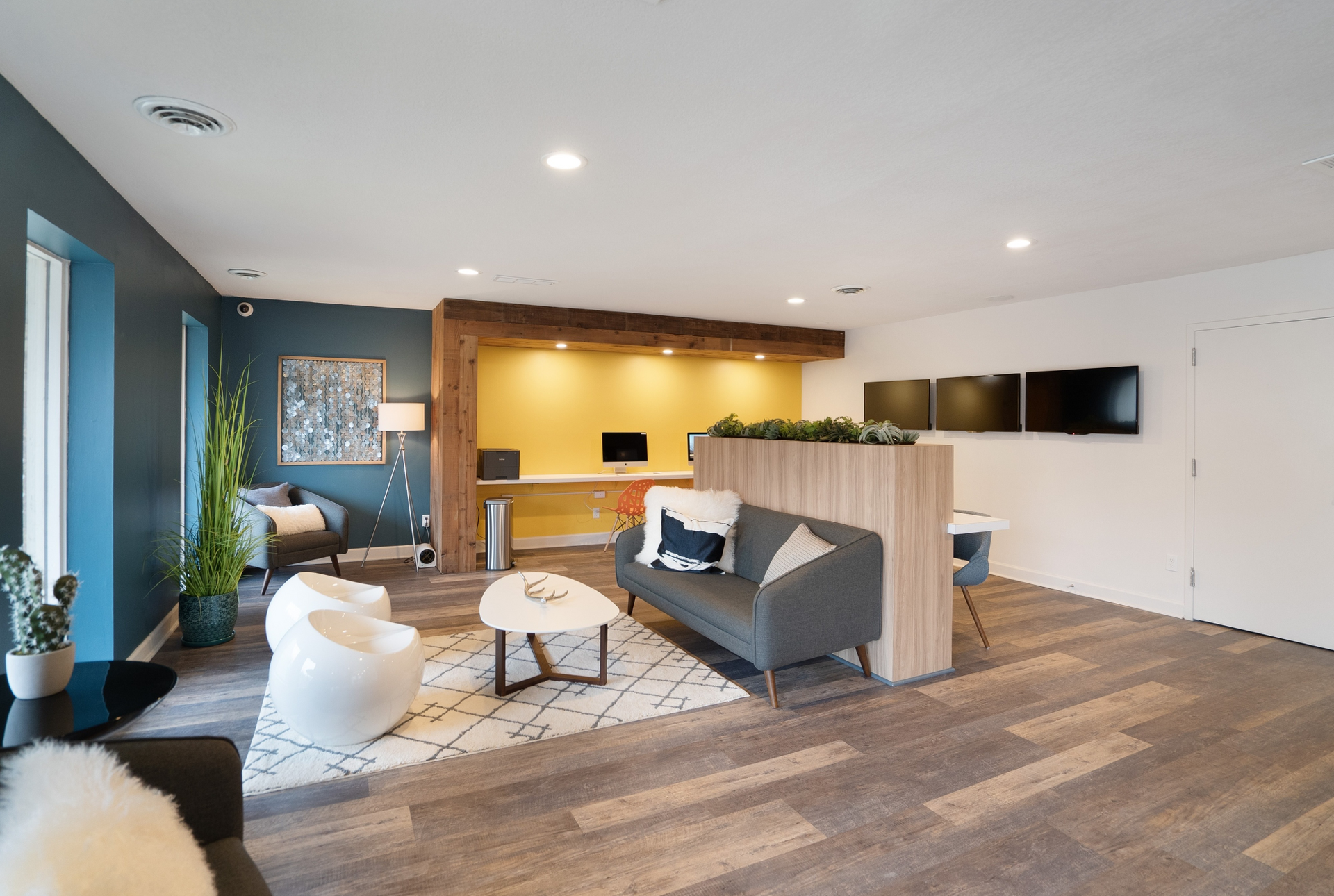 Modern apartment community lounge with seating, plants, and wall-mounted monitors.