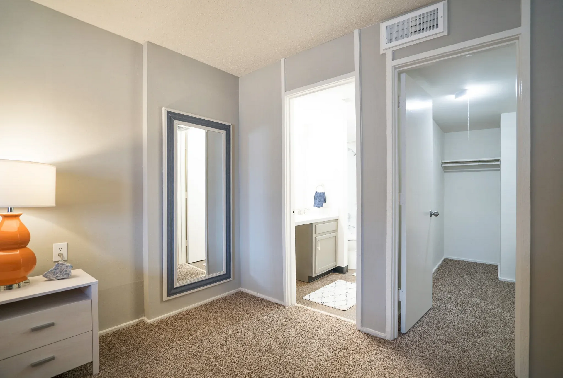 Bedroom corner with carpet, a large wall mirror, and open bathroom and closet doors.