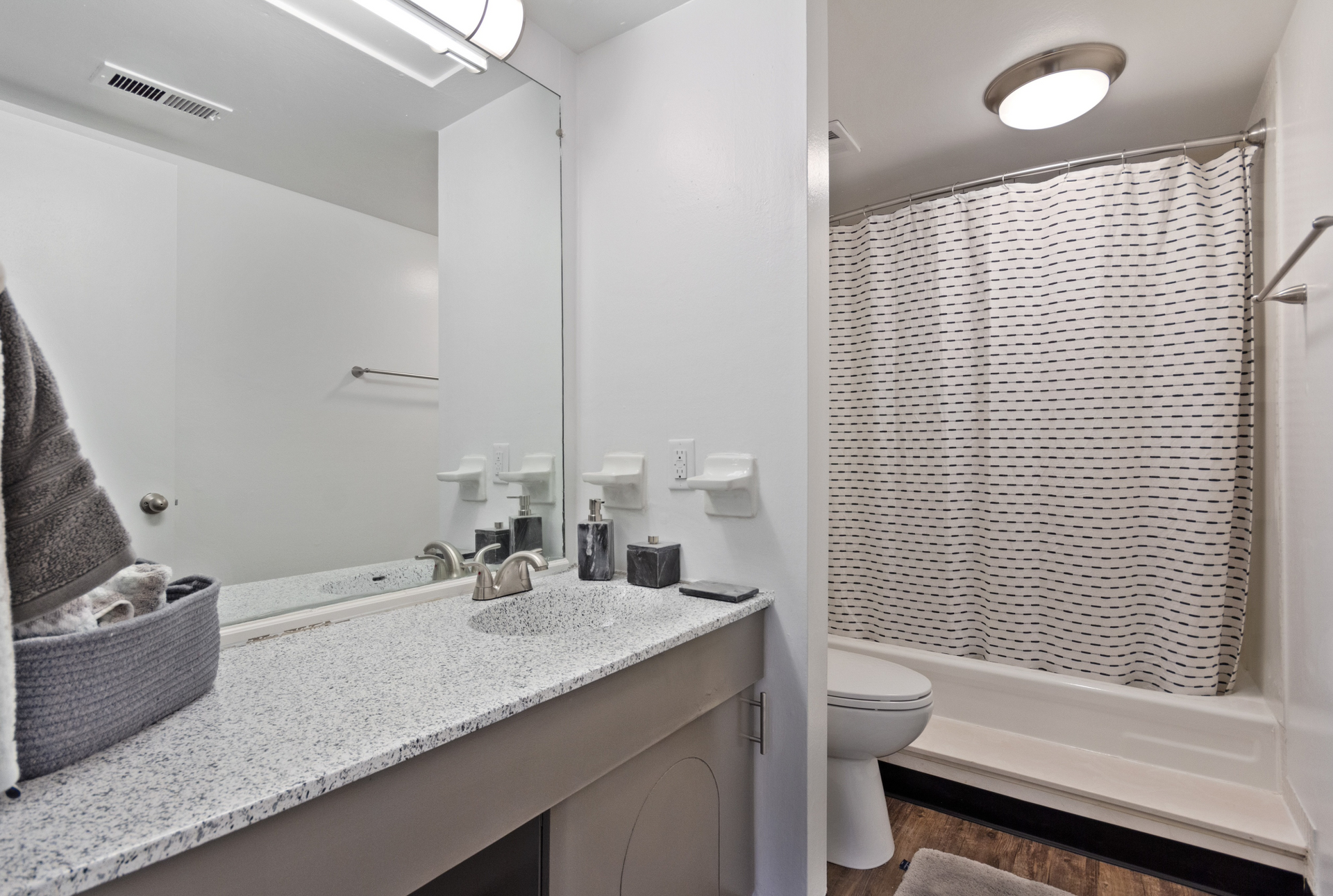 Bathroom with single vanity, mirror, toilet, and bathtub with a striped shower curtain.