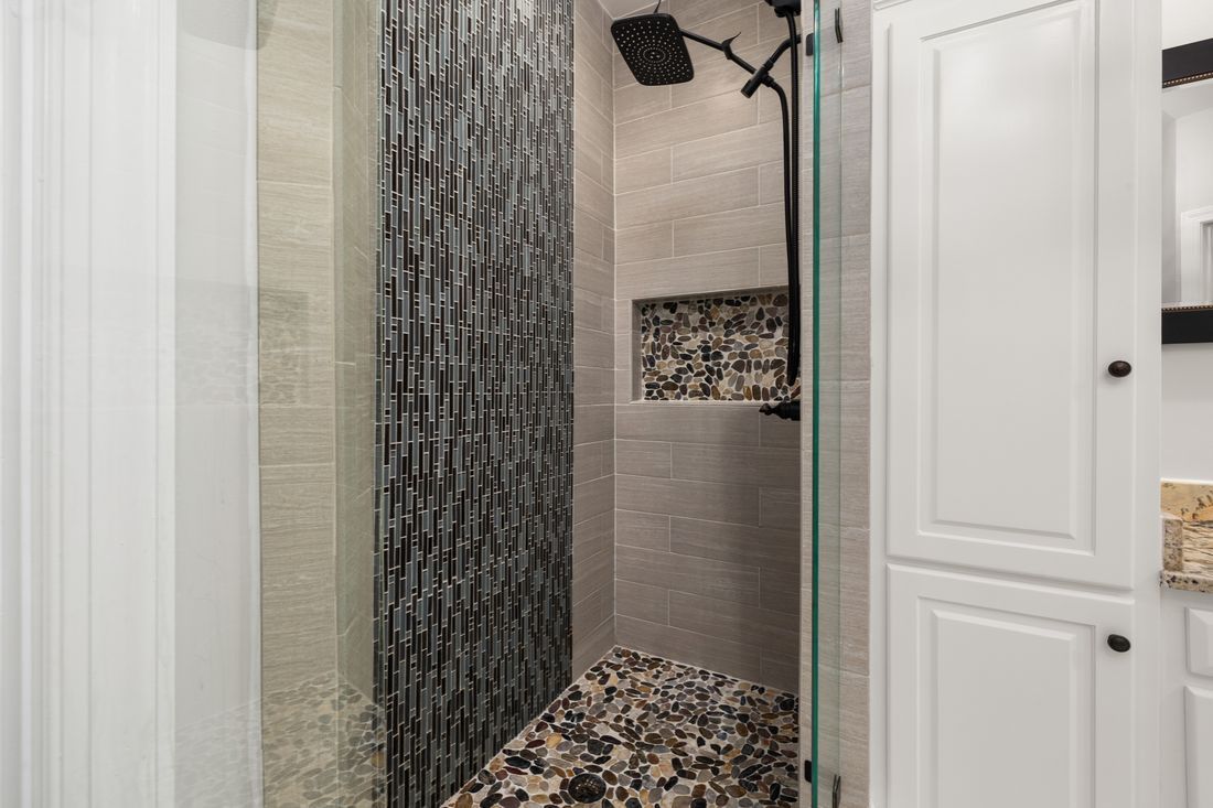 Modern shower with dark mosaic tile, built-in niche, and glass door in a white bathroom