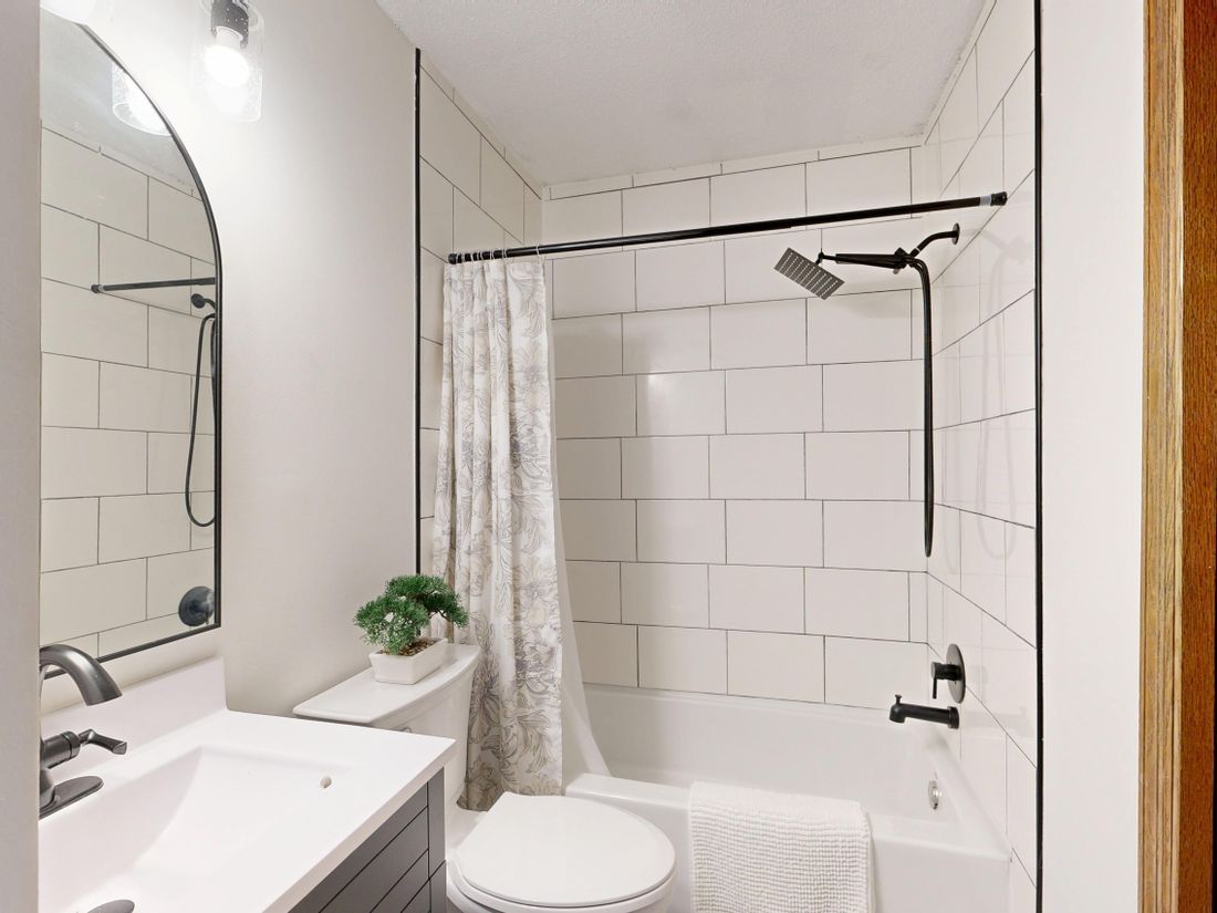 Bright white bathroom with tub, shower curtain, sink, toilet, and round mirror