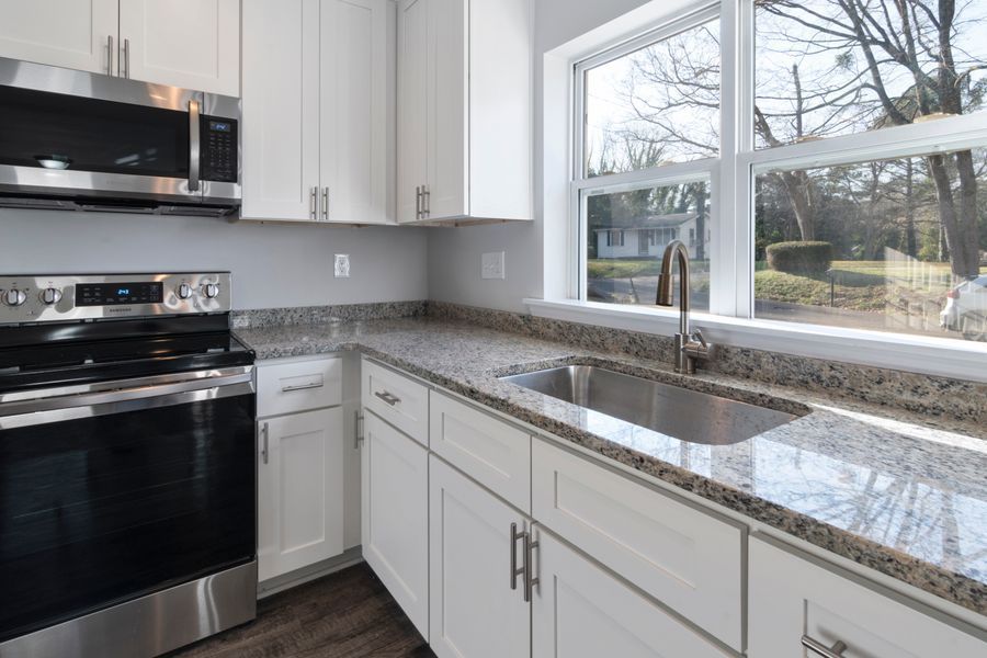 Bright modern kitchen with white cabinets, black appliances, and granite countertops by a large window