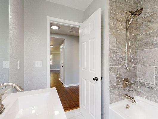 Bright bathroom with a tub, tiled shower, and open door to a hallway with wood floors.