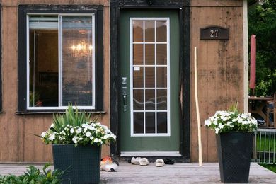 Front door of a brown house with two black planters of white flowers on either side