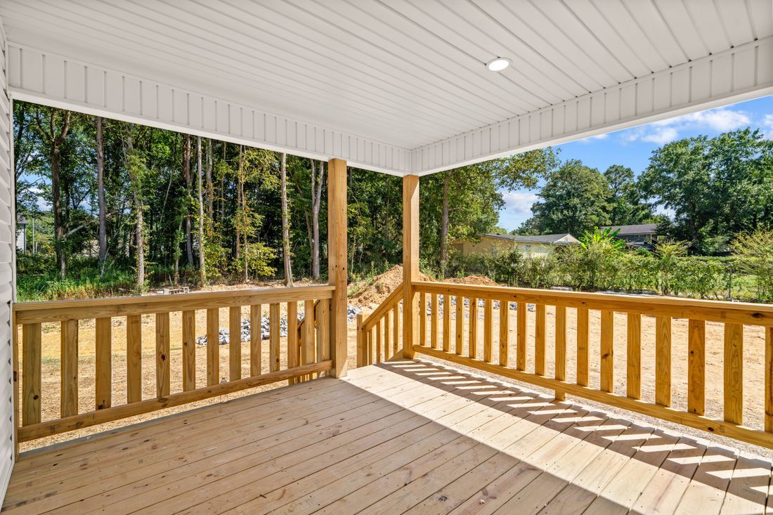 Covered wooden porch with railing overlooking a sunny grassy yard and trees