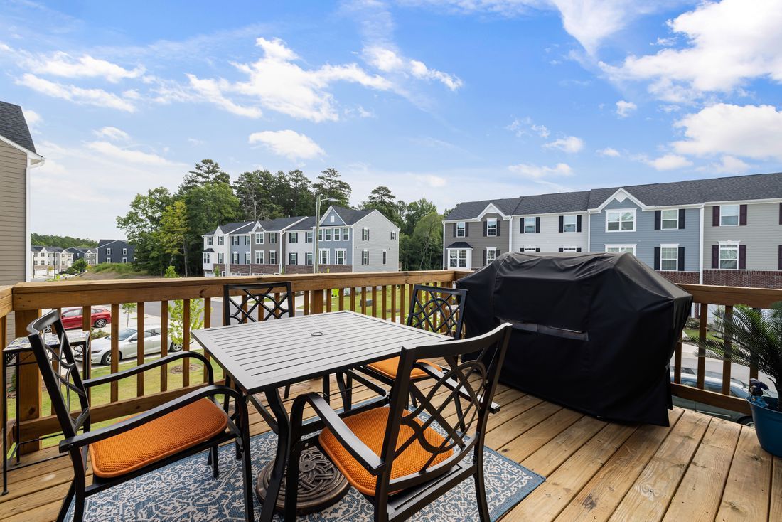 Balcony deck with table, chairs, grill, and view of apartment buildings under a blue sky