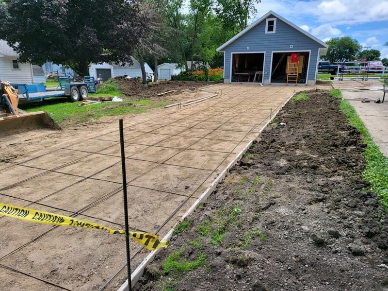 Construction site with rebar forms for a new concrete driveway leading to a gray garage.