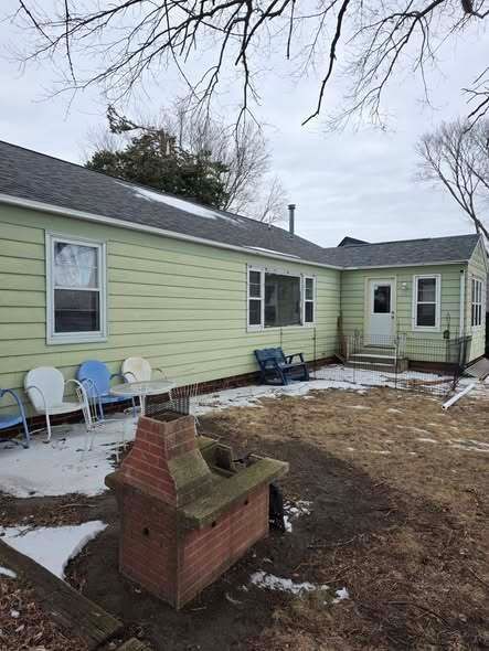 Backyard with pale green house, patio chairs, and a brick grill in winter snow