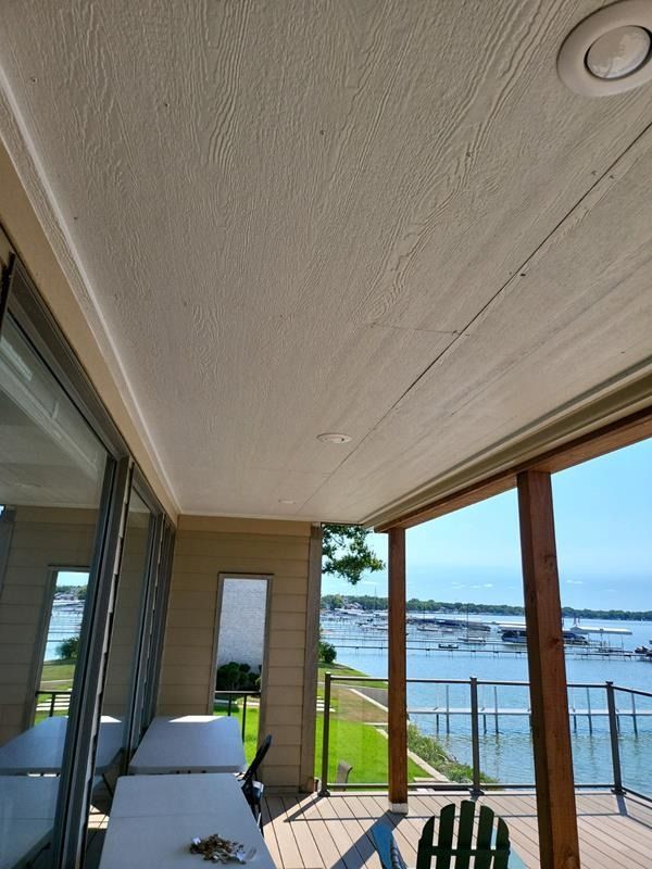 Covered waterfront patio with lounge chairs, glass railing, and ocean view beyond the deck
