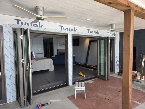 Open patio doors in a partially finished building with tools and a small stool outside.