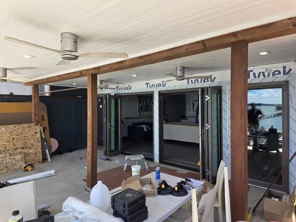 Covered patio renovation with exposed beams, sliding doors, and construction materials scattered around