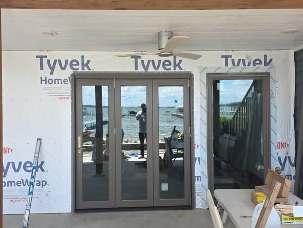Tyvek-covered house entry with double glass doors and an ocean view beyond the patio.