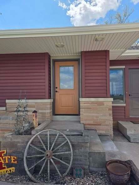 Front entry of a house with red siding, tan stone trim, wooden door, and wagon wheel decor.