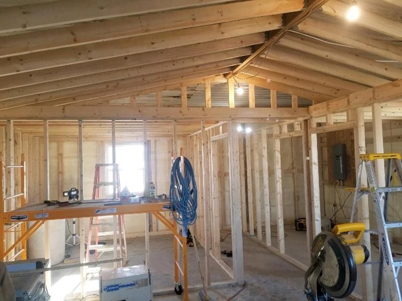 Interior of a framed house under construction with exposed wooden rafters, tools, and scaffolding.