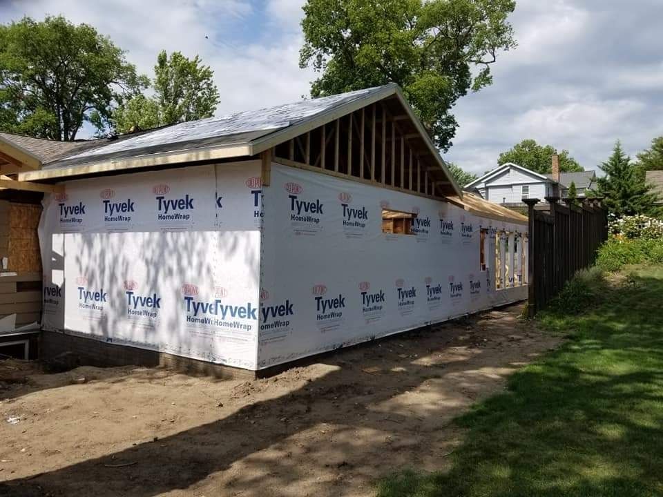 Partially wrapped house under construction with Tyvek house wrap and a metal roof, beside a dirt path