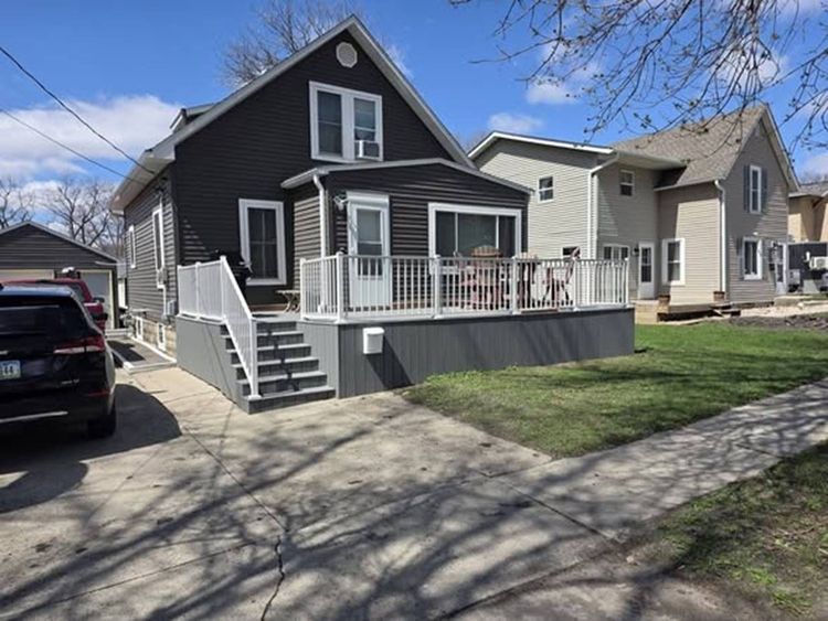 Dark gray house with white porch and steps on a sunny residential street