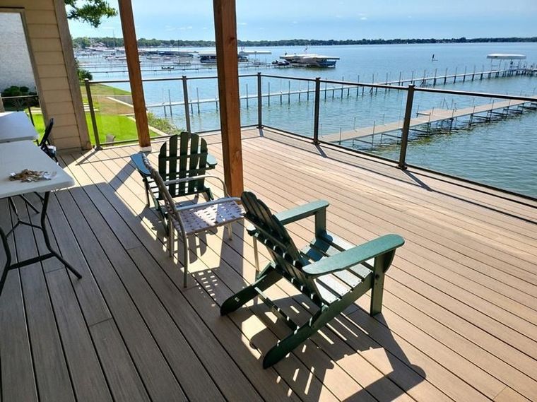 Wooden deck with Adirondack chairs overlooking a calm waterfront and dock on a sunny day
