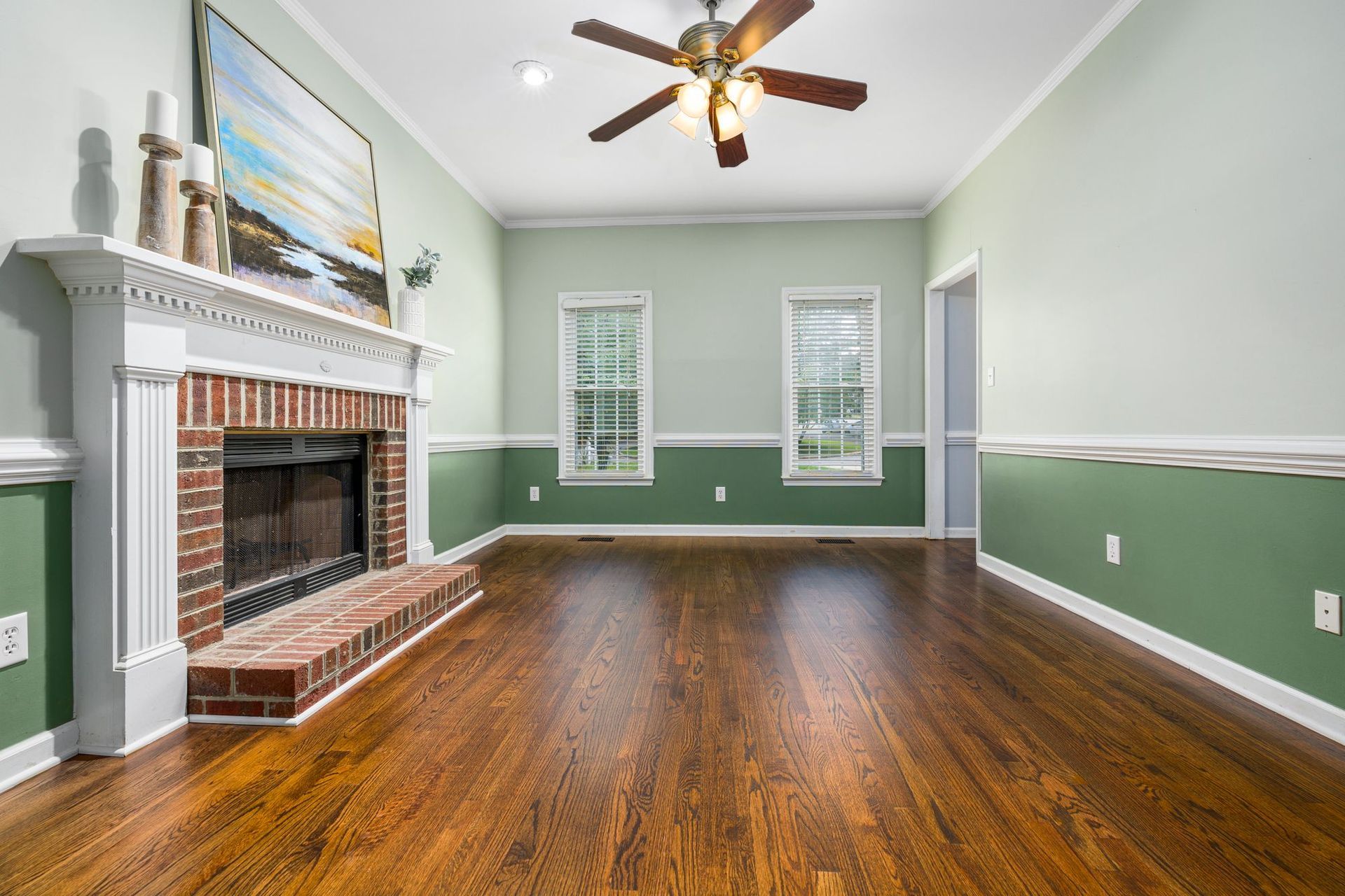 Empty living room with green walls, hardwood floor, brick fireplace, and ceiling fan