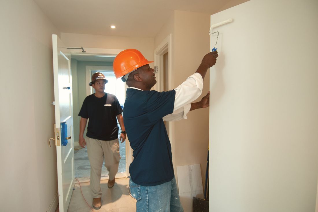 Two workers in hard hats inspect a hallway wall during home renovation