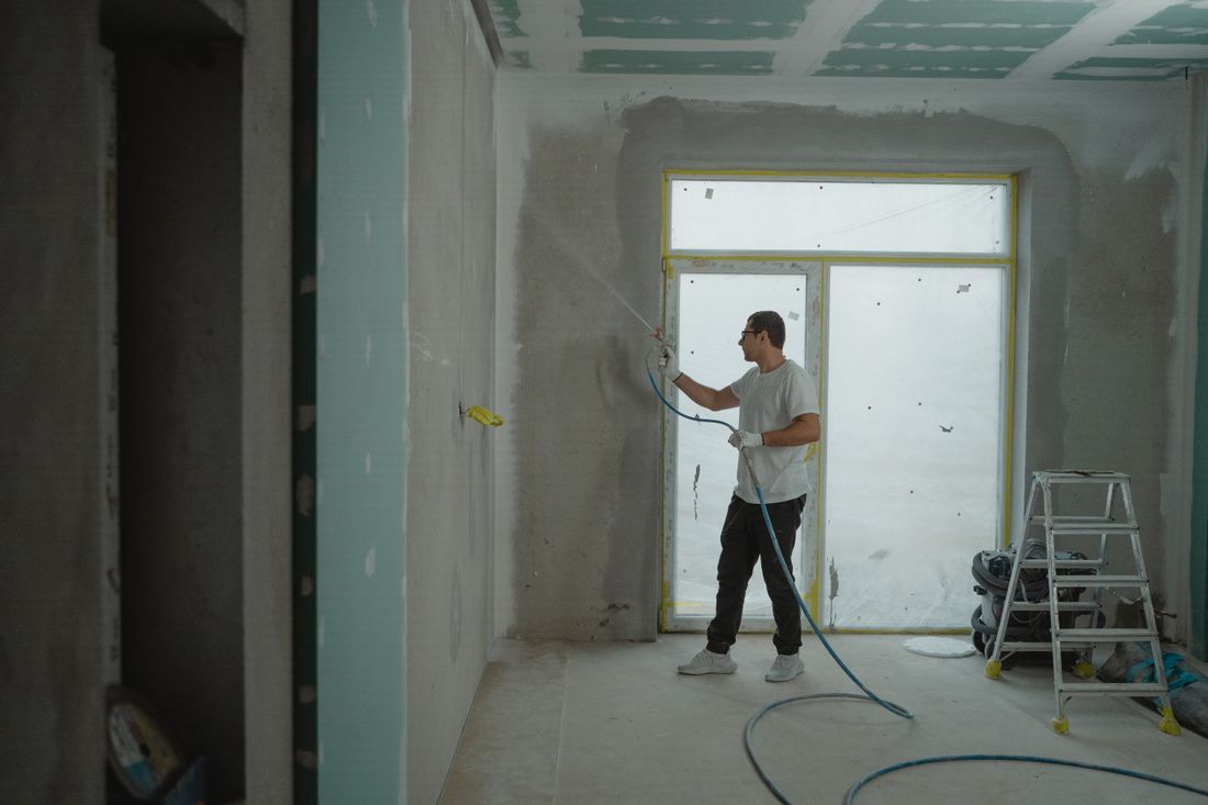 Person painting a room under renovation, with a ladder and paint supplies nearby.