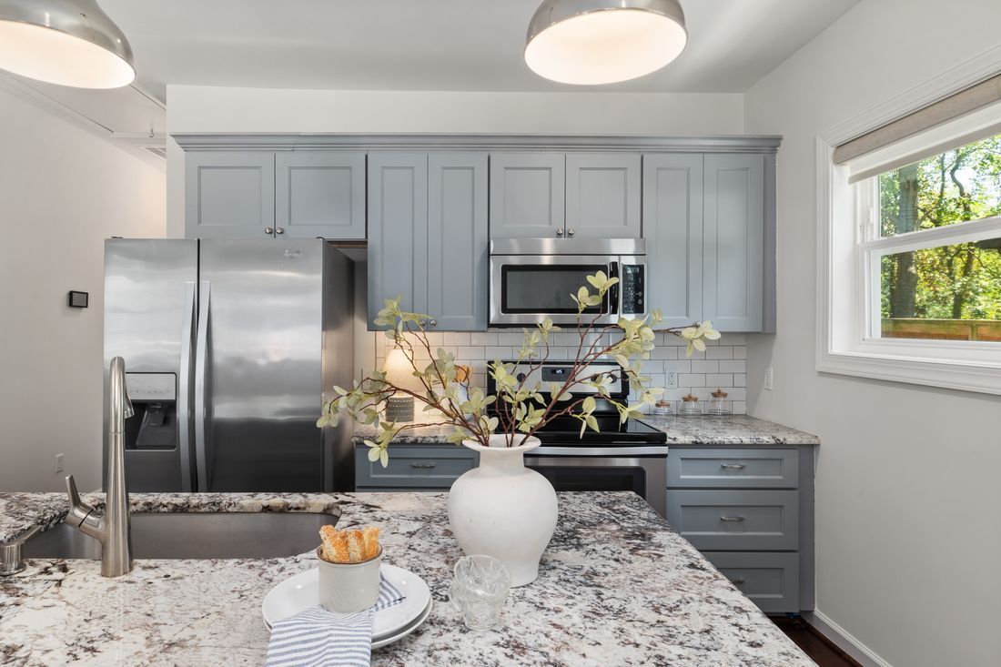 Modern kitchen with gray cabinets, stainless steel appliances, and a granite island with a vase of flowers.