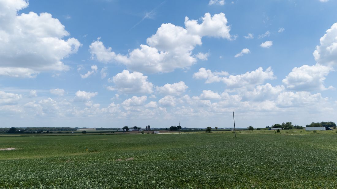 Wide green field under a bright blue sky with scattered white clouds and a distant horizon