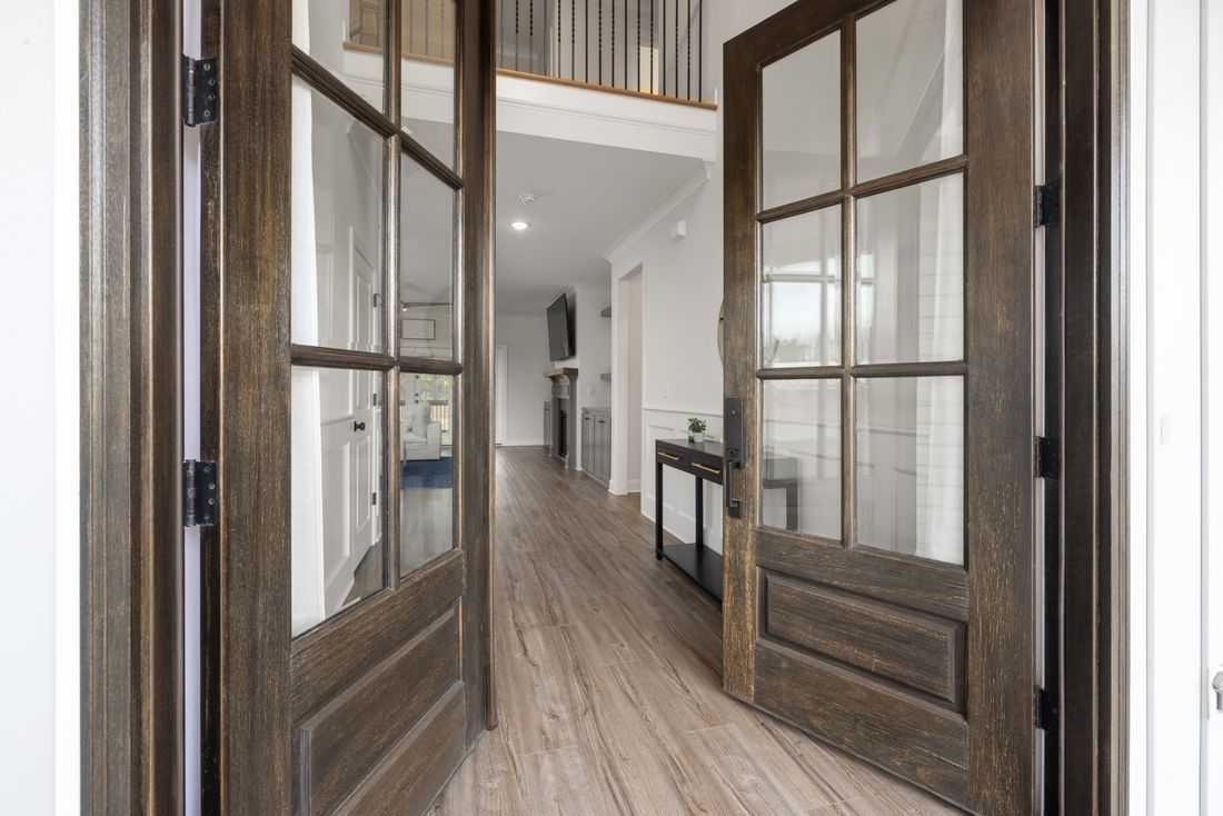 Open wooden double doors leading into a bright hallway with wood floors and glass partitions
